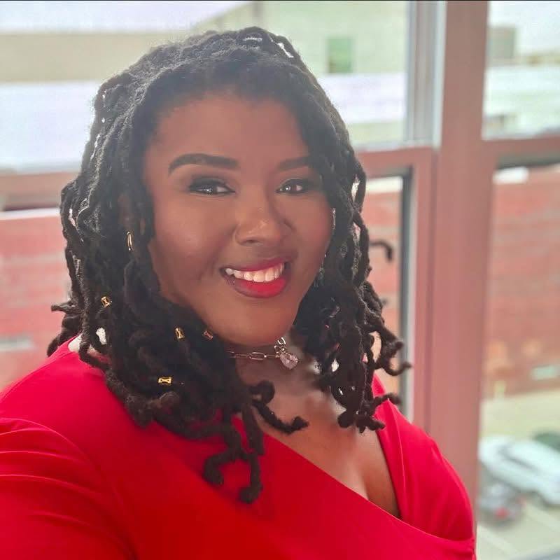 Dr. Ashley Dash smiling in a red dress beside a window